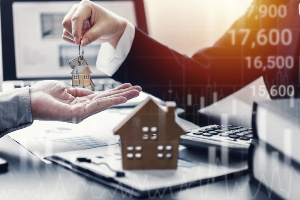 Hand passing house keys over a model house and a calculator